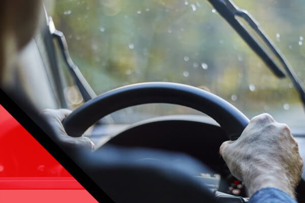 Back view of a man driving a car with moving windshield wipers during rain.